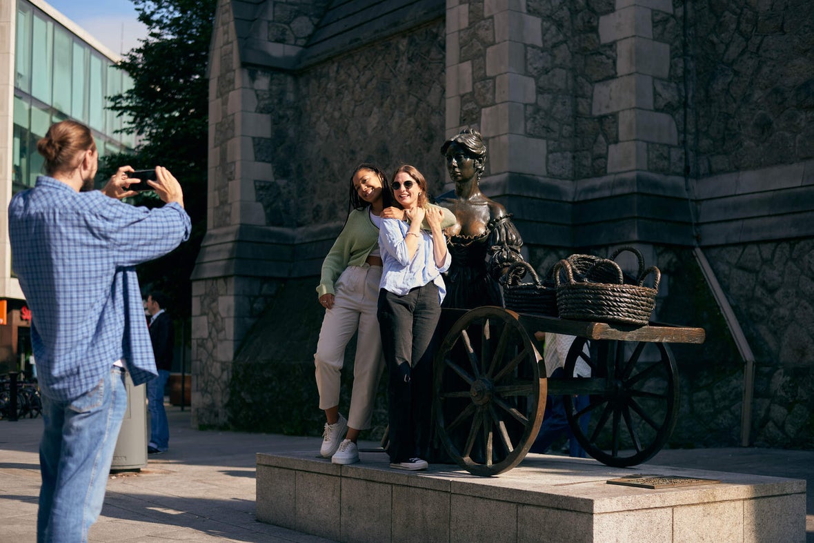 A group of friends posing with the Molly Malone statue while another friend takes their picture.