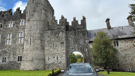 Silver car parked on a driveway with a castle in the background