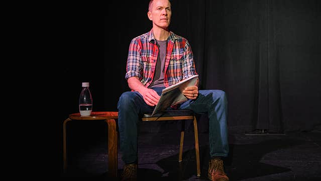a man in checked shirt seated on a chair on stage