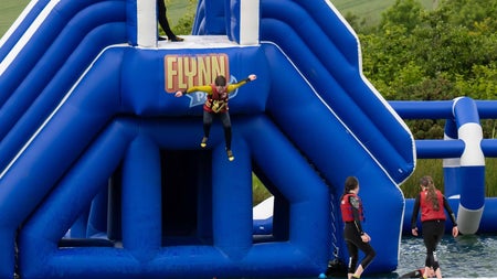 Large blue outdoor inflatable water obstacle course with people in red life jackets