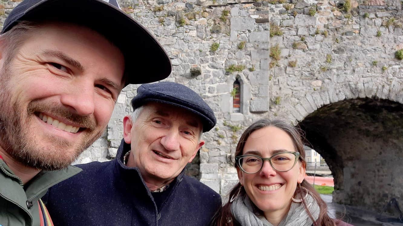 Three people smiling standing to the side of a stone archway