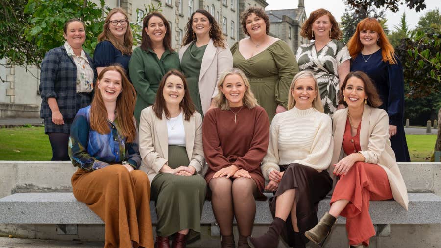 enCÓRe at Christmas, a group of smiling women seated on and standing behind a concrete bench outside a building