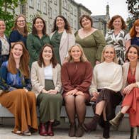enCÓRe at Christmas, a group of smiling women seated on and standing behind a concrete bench outside a building