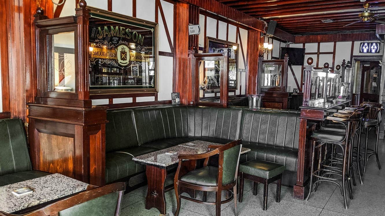 Pub with green leather chairs and seats and wooden tables and the bar with bar stools towards the back