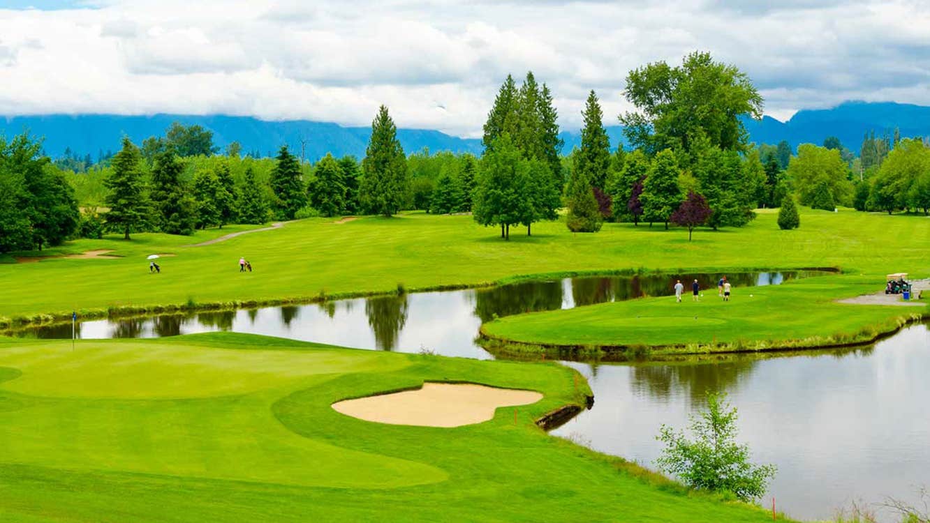 Golf course with trees sand bunkers a lake and players on the green