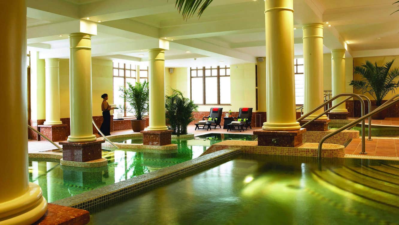 A large room in a spa with tall pillars and a pool