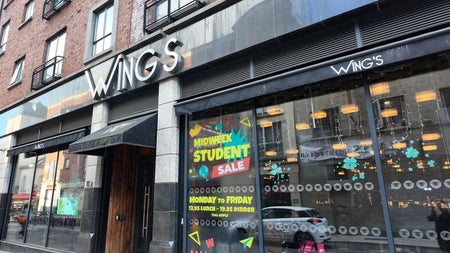 Exterior of a restaurant with lots of windows and black awning over a wooden door
