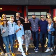 Group posing in front of a red and black building some holding drinks