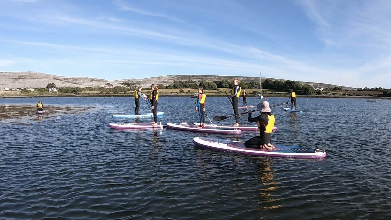 Group in yellow lifejackets on pink paddle boards at sea