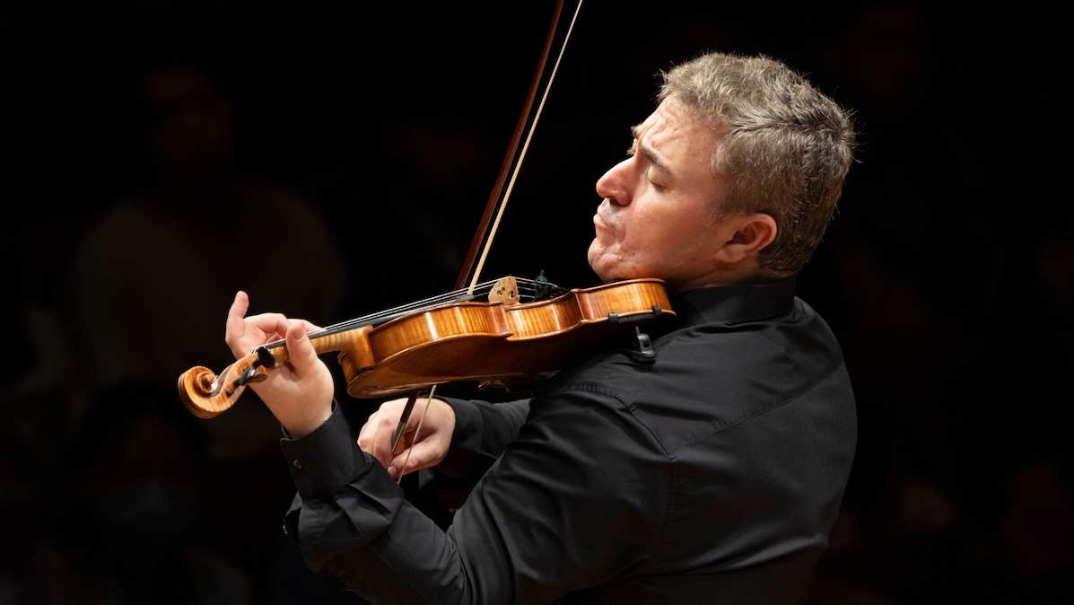 Side view of a man playing a violin with emotion, against black plain background.