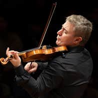 Side view of a man playing a violin with emotion, against black plain background.