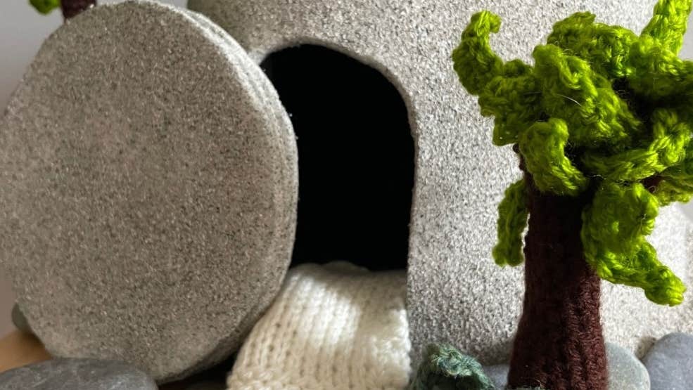 A stone tomb, open, with knitted trees and smaller stones surrounding it.