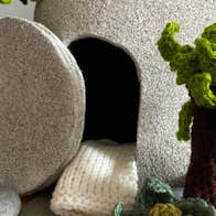 A stone tomb, open, with knitted trees and smaller stones surrounding it.