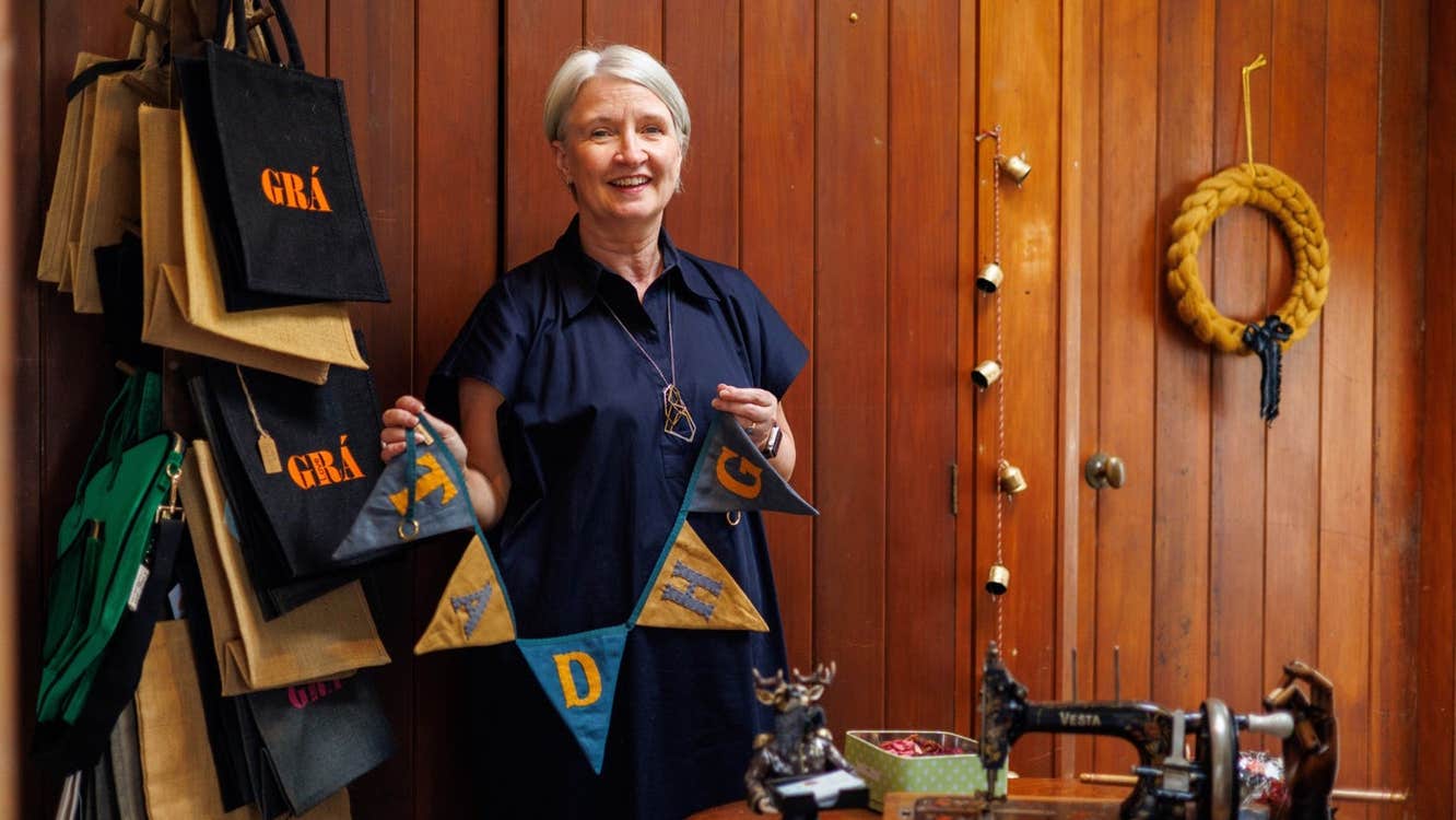 A lady standing in a workshop beside a sewing machine holding linen bunting