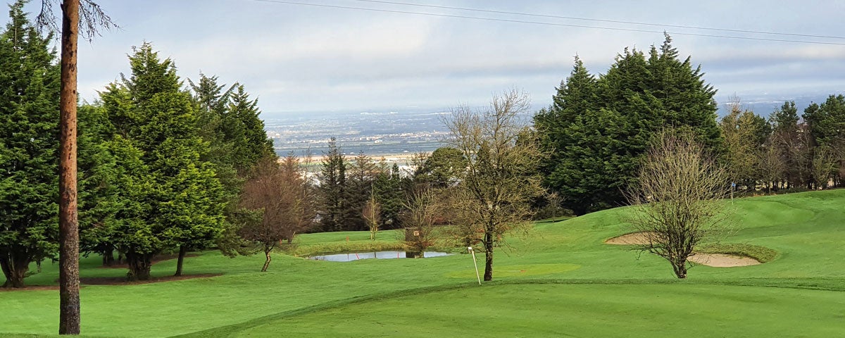 One of the greens with two bunkers to the right and small lake in the centre and view of Dublin City in the background