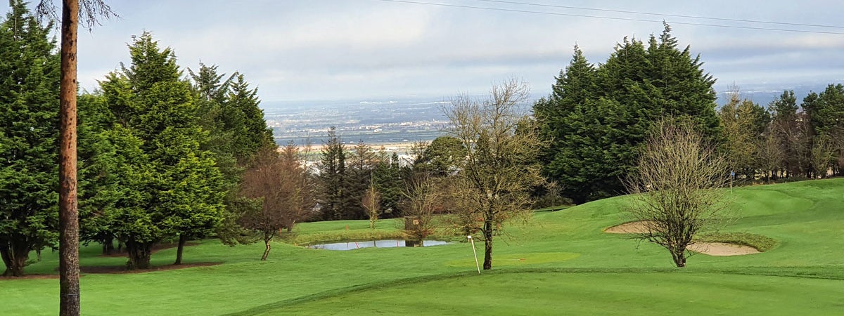 One of the greens with two bunkers to the right and small lake in the centre and view of Dublin City in the background