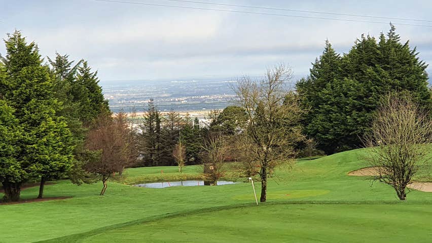 One of the greens with two bunkers to the right and small lake in the centre and view of Dublin City in the background