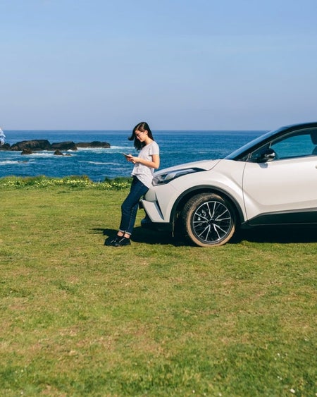 Two people at a coastal location beside a car