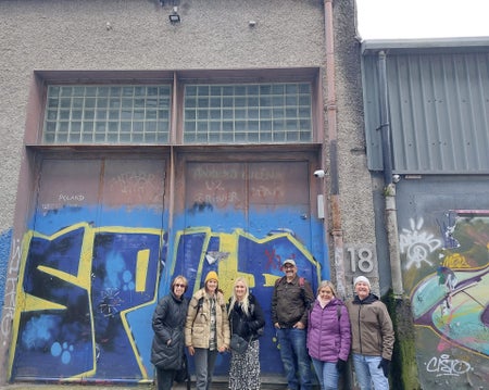 Six people in front of a building with blue and yellow doors and the number eighteen on it