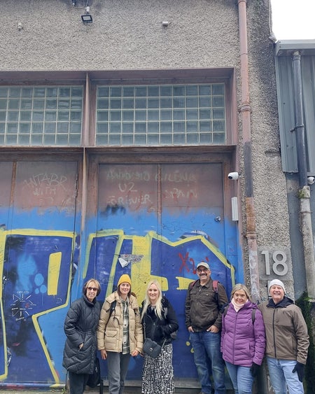 Six people in front of a building with blue and yellow doors and the number eighteen on it