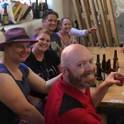 Six people holding glasses sitting at a wooden table with beer bottles on it