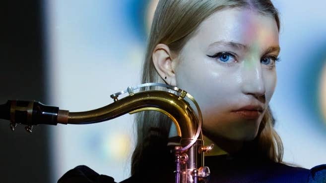 A head and shoulders view of a serious woman holding a saxophone upright in front of her.