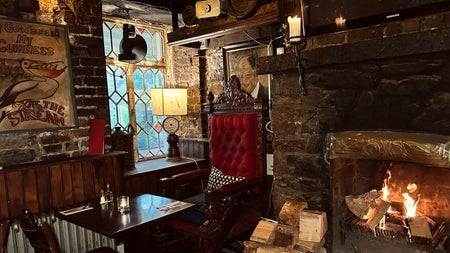 Stone interior of a pub with a lighting wood burning fire and table set for service