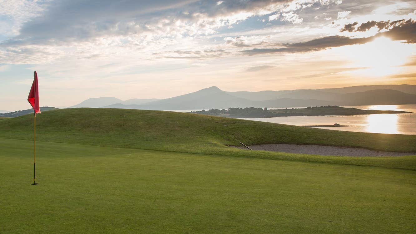 Red flag on a golf course overlooking the water at sunset