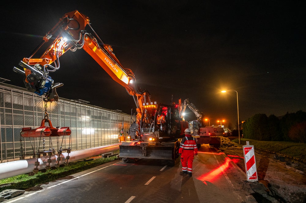 man in oranje overall naast werkvoertuig