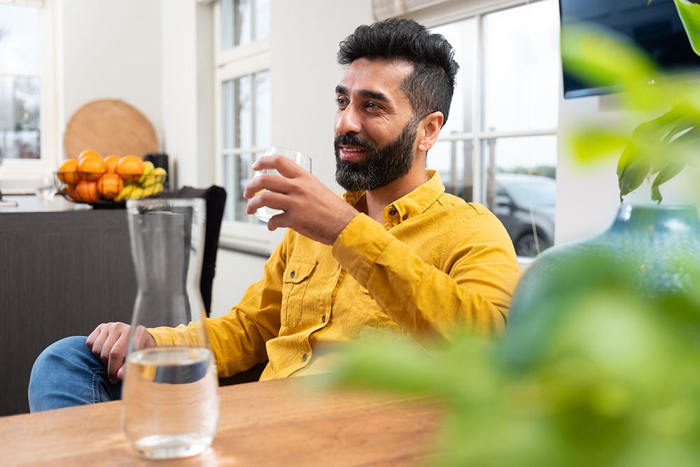 Man aan keukentafel met glas water in zijn hand