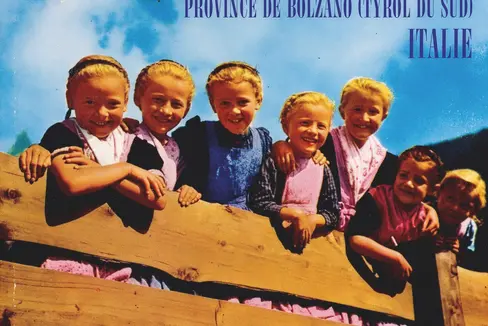 In den 1970er Jahren wurde Südtirol touristisch als idyllische Heimat für die Gäste inszeniert – mit traditionellen Motiven wie Bergen, Obstgärten, Bauernhäusern und Trachten. Im Bild „Eingeborene“ in Tracht, Prospekte und Plakate vermitteln ein traditionsbetontes Südtirolbild. (Foto: Touriseum)