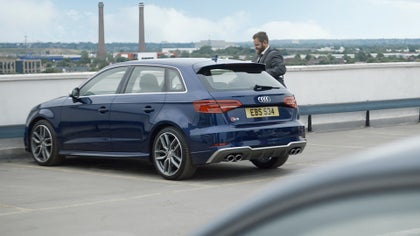 A guy next to a blue Audi S3 in a car park.