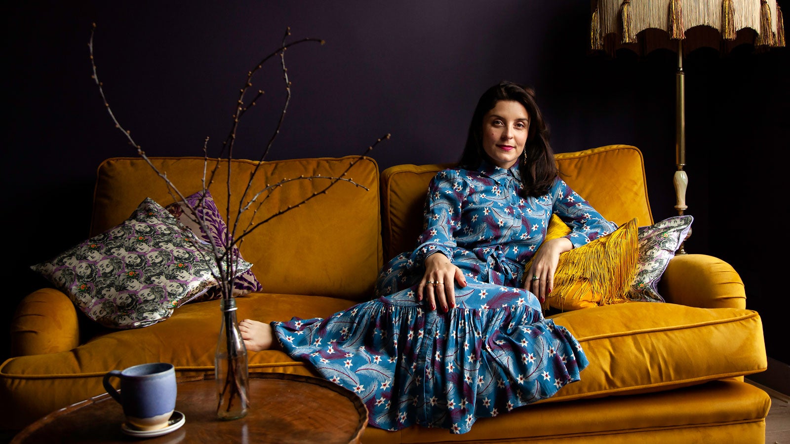 Jessie Burton sits in a blue dress on a yellow velvet sofa