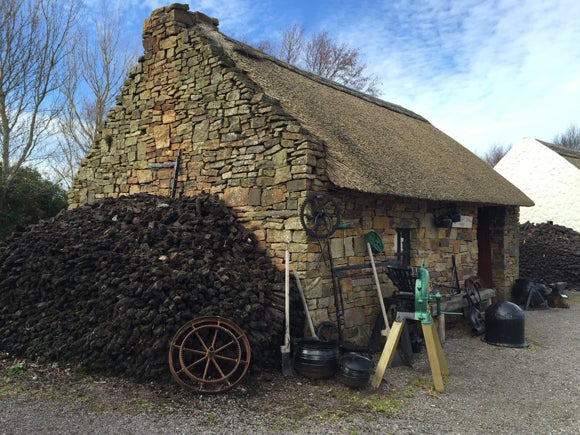 A recreated blacksmith’s forge: a small stone cottage with a thatched roof and tools outside on a gravel path