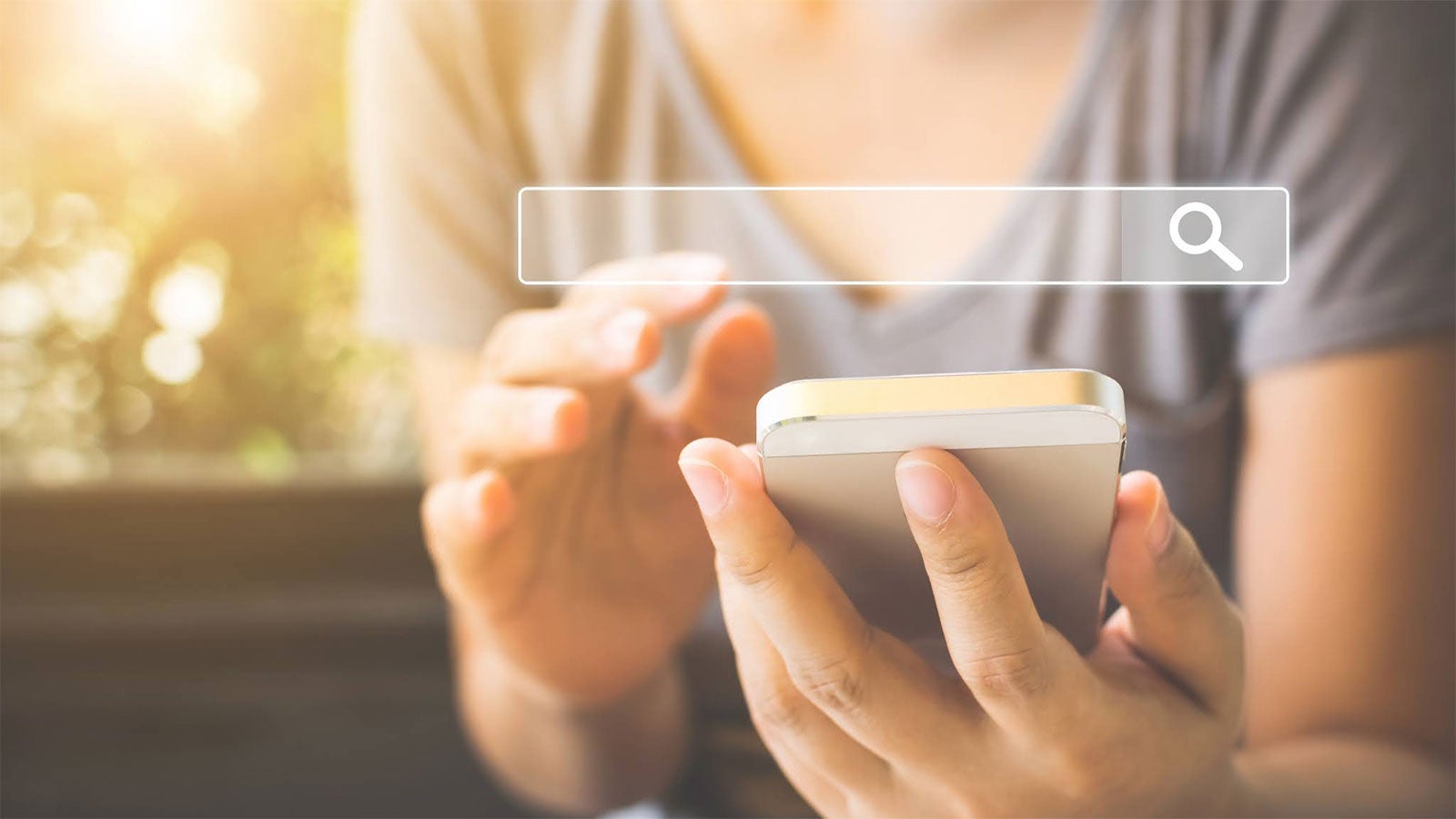 A woman holds a mobile phone, she is about to type something into a blank search field.