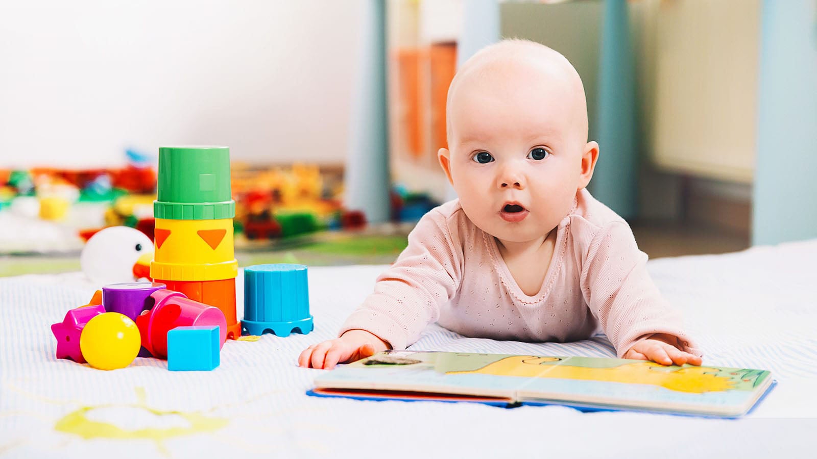 Baby led on floor with an open book and stacking toys
