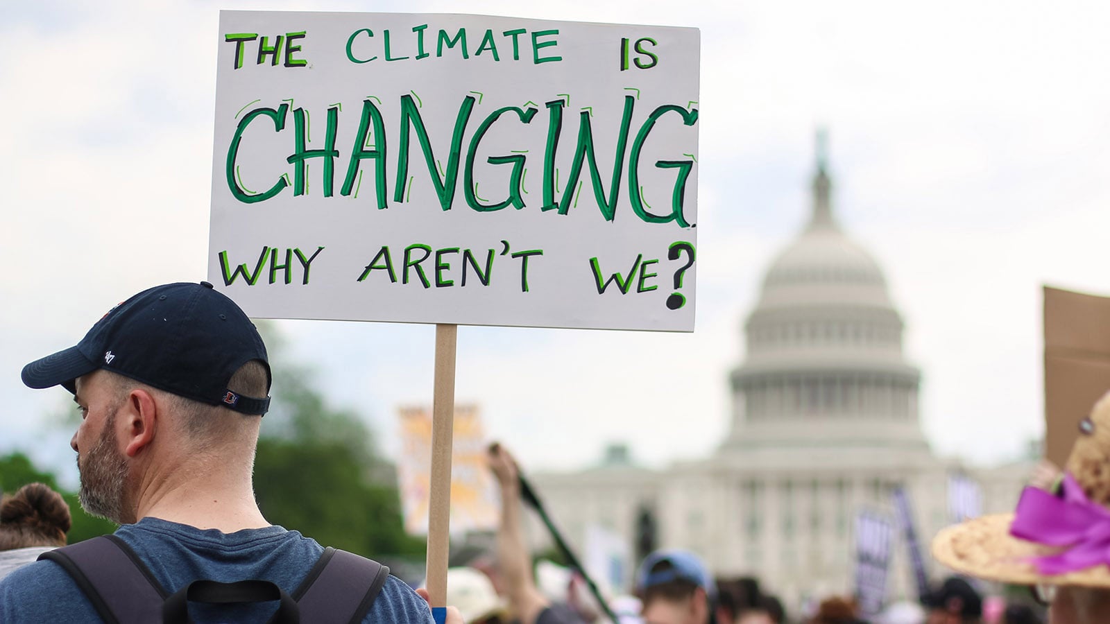 Man holding placard which says The Climate is Changing Why Aren't We?