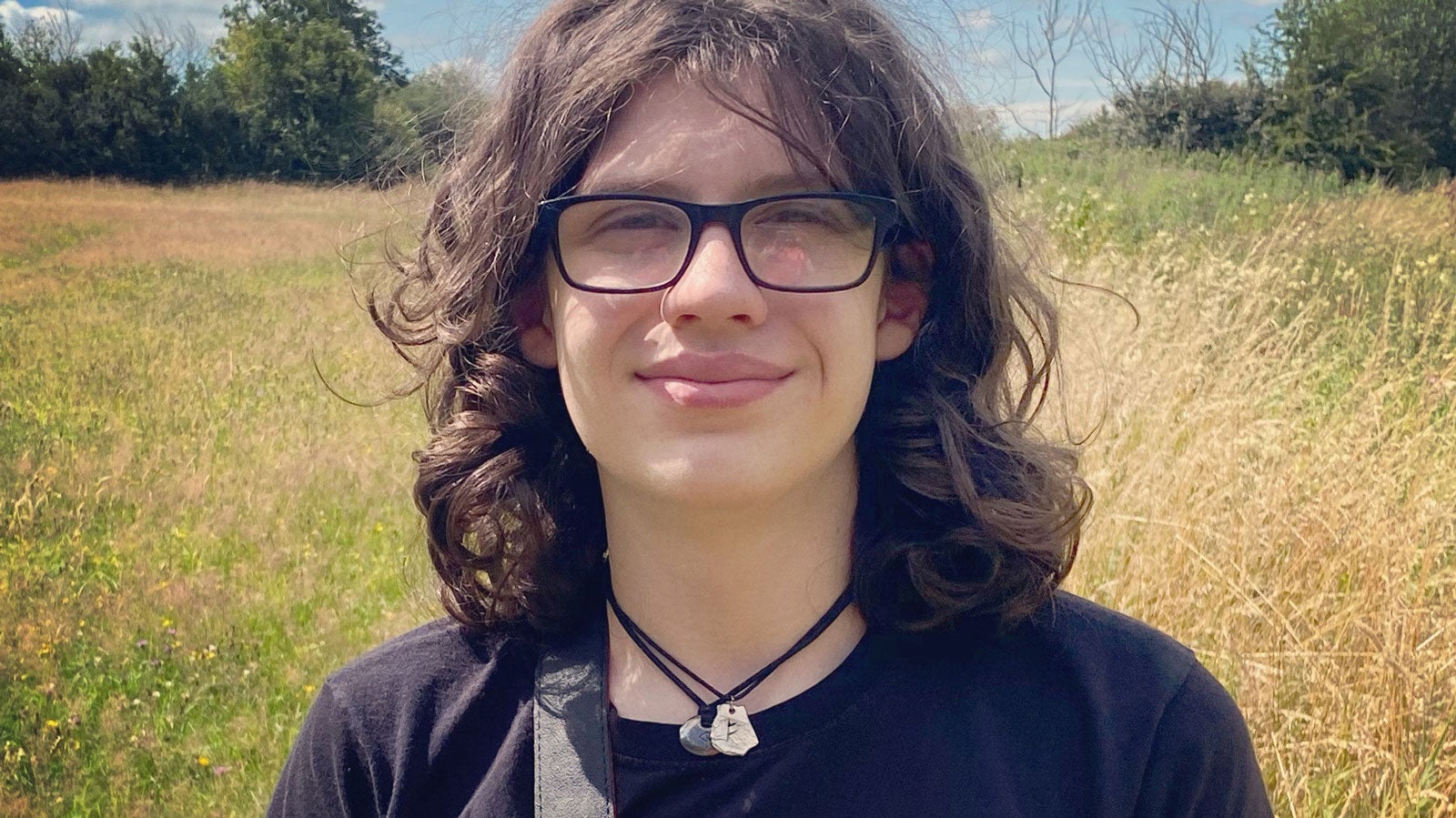 Dara McAnulty wears a black t-shirt and smiles in a summer field