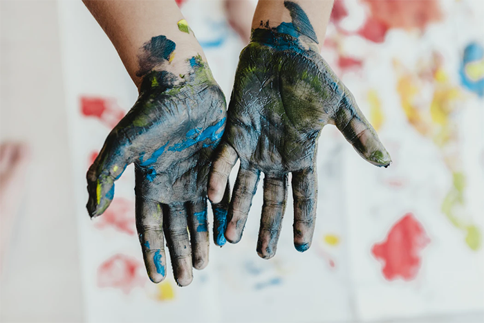 child's hands covered in various colours of paint with blurry creations in background