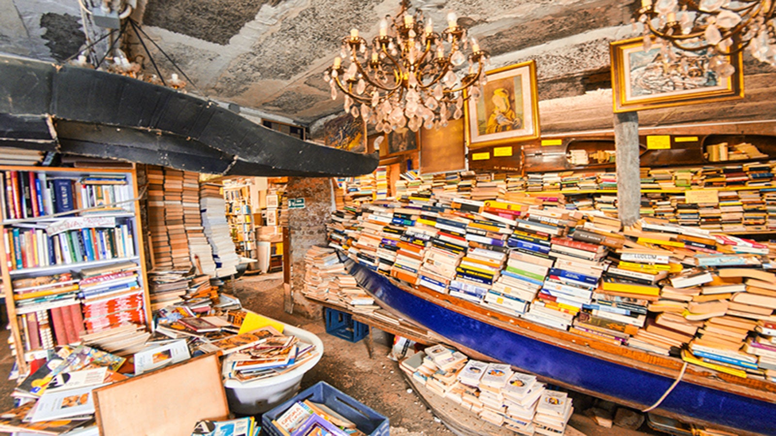 a crowded second hand bookshop wth a row-boat crammed full of books n the centre of the room