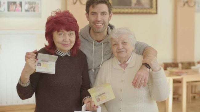Larysa, Zac & Kateryna stand with arms around each other smiling to camera as Larysa and Kateryna hold their visas
