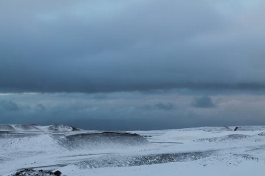 An expansive, snow covered, rocky and barren landscape with dark grey clouds rolling above