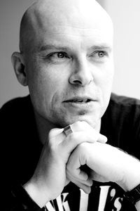 Black and white photograph of Adam Nevill resting his head on his hands.