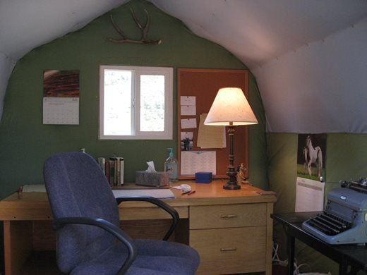 writing desk in a cosy room with a green wall, a lamp on the desk and a typewriter to the right-hand side