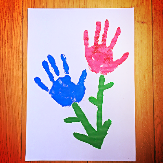 A child's painting featuring a blue and a pink hand impression, in the shape of a couple of flowers.