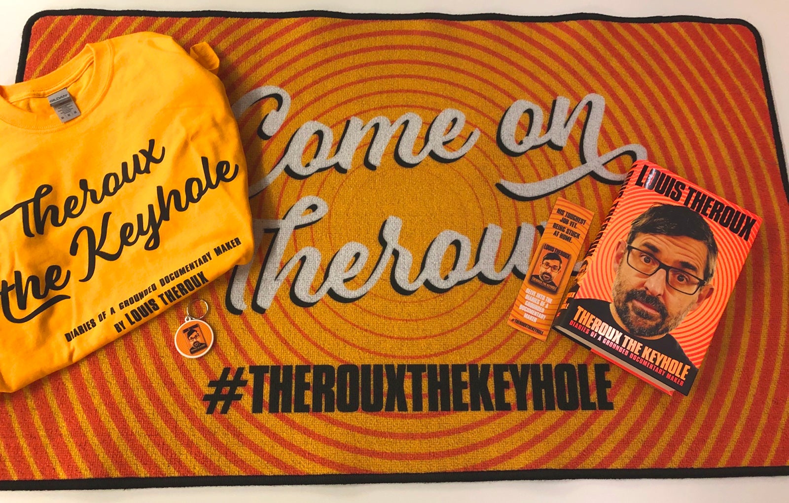 A copy of Theroux the Keyhole, a themed keyring, t-shirt and bookmark all sit atop a themed doormat. A copy of Theroux the Keyhole, a themed keyring, t-shirt and bookmark all sit atop a themed doormat.