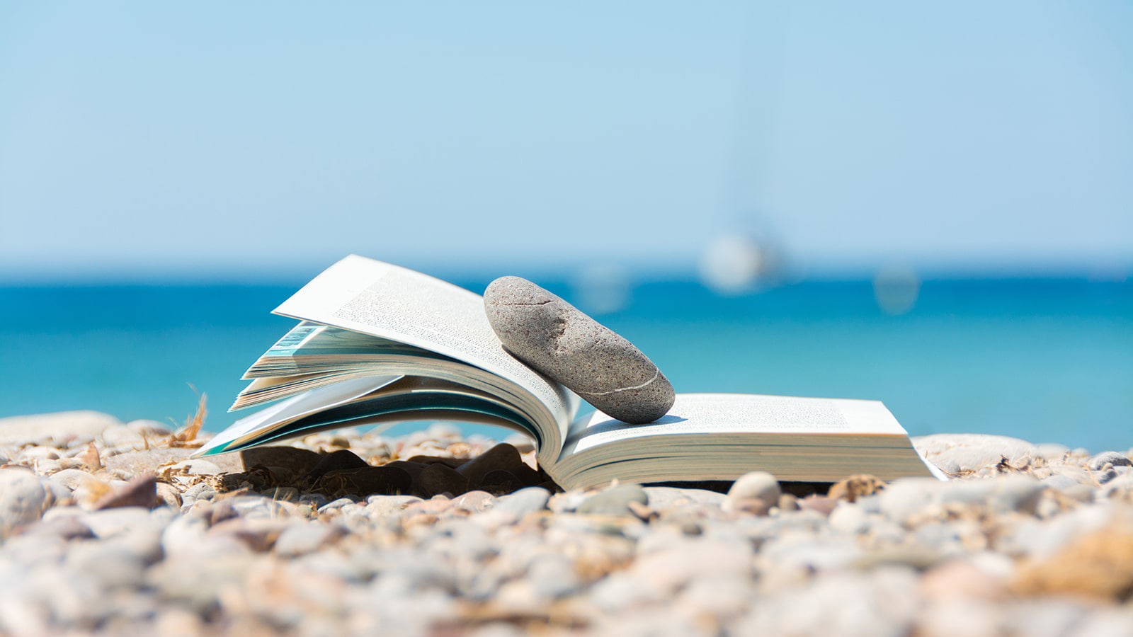Open book on a pebble peach with blue sky