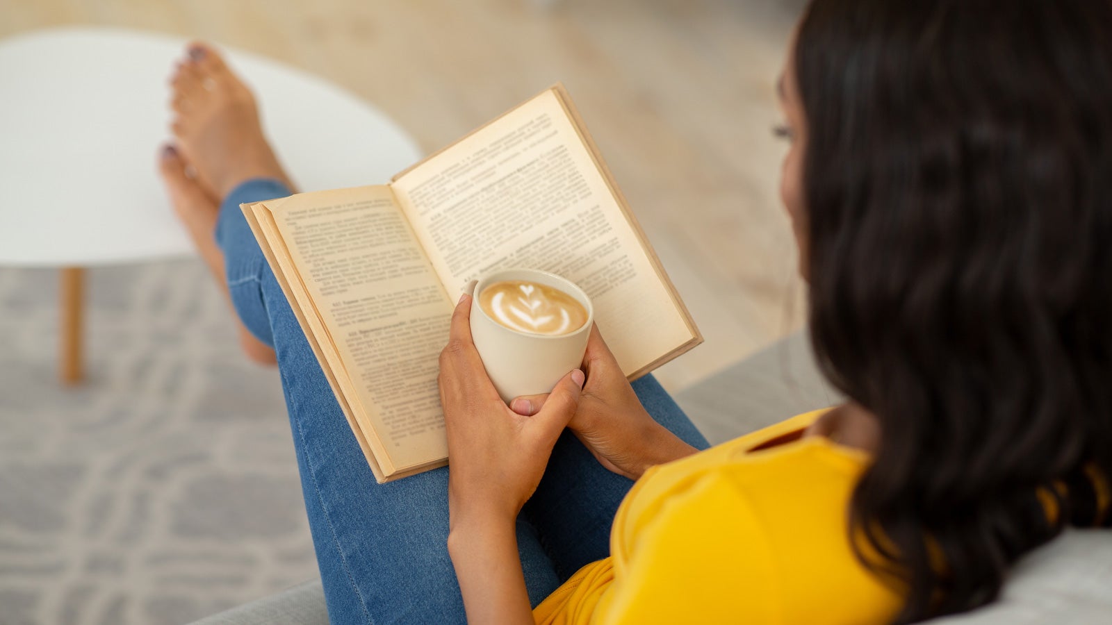 Woman reads with her feet up on a coffee table holding a coffee