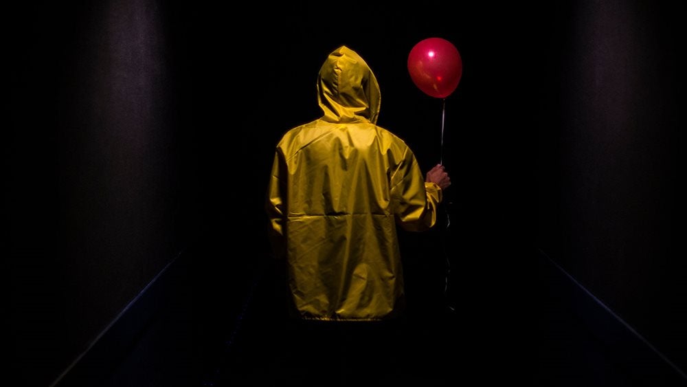A person wearing a yellow rain jacket holding a red balloon