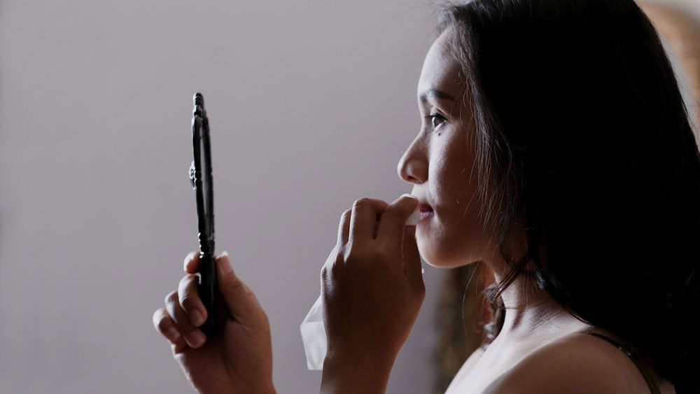 Woman looking in mirror holding tissue